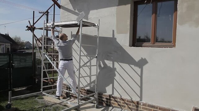 construction worker on ladder smoothing plaster