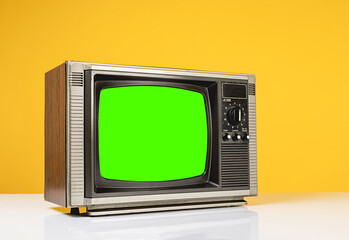 Old retro TV with chroma key green screen on white table with on yellow background, side view.
