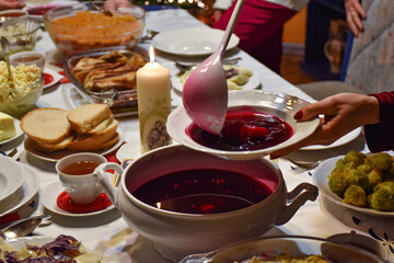 A traditional Polish Christmas dinner with barszcz czerwony (beetroot soup) served with uszka (small dumplings), bread, tea, fried fish, and vegetables on a festive table with a lit candle.