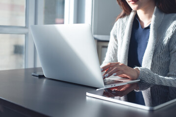 Asian business woman working, typing on laptop computer at home office with digital tablet on table. surfing the internet, searching the information, remote work, telecommuting