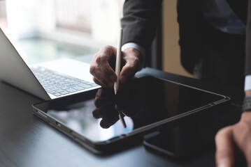 Closeup of businessman using stylus pen signing e-document on digital tablet and working on laptop...