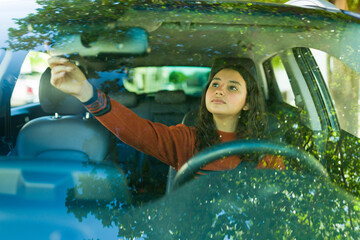 Teenage driver adjusting the rearview mirror on a sunny day