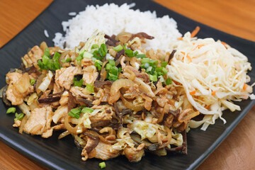 Oriental dish: spaony chicken, vegetables, sweet and sour sauce, salad and rice on a plate stands on the table.
