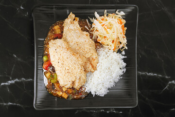 Oriental dish: crispy panko-coated chicken with vegetables, salad and rice on a plate stands on the table.