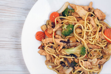 Oriental dish: Asian noodles with vegetables and chicken on a plate stands on the table.