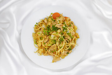 Oriental dish: Asian noodles with vegetables and chicken on a plate stands on the table.
