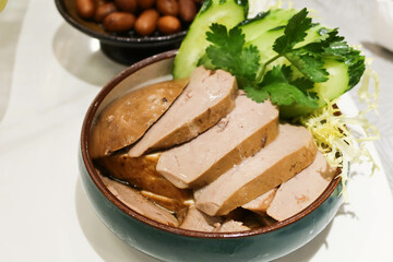 close up of Chinese Hong Kong Chaozhou style marinated goose liver foie gras slice with cucumber on the side in a blue bowl
