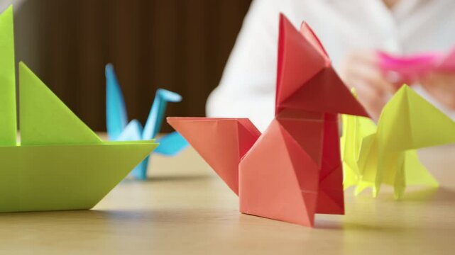 Woman's hands folding origami colored paper on table. Hobby, handmade and decor concept.