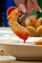 A person is savoring a crispy fried shrimp, dipping it into a tangy sauce