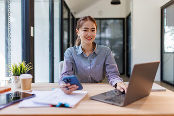 Business Asian woman hold phone and use laptop at the workplace. Project stats financial data sales charts on laptop and cellphone Asian finance concept
