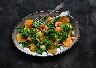 Delicious snack salad with shrimp, avocado, arugula and tangerines on a dark background, top view