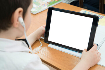 .A child using a tablet with earphones, sitting at a wooden desk. The screen displays a gradient blue background. Ideal for education, technology, or digital learning themes.