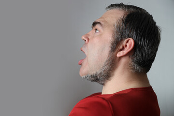 Obraz premium Wow, amazing! Side view of astonished man in casual red t-shirt standing with mouth open in surprise, scared and shocked by crazy unbelievable news. studio shot isolated on white grey background