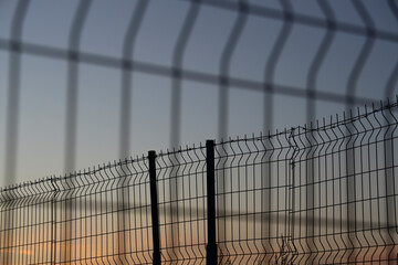 Obraz premium Barbed wire net Fence Sunset against blue sundown sky background. sunset behind the wires. Mesh Steel and Barbed Wire, Sunset with Red and blue heaven.
