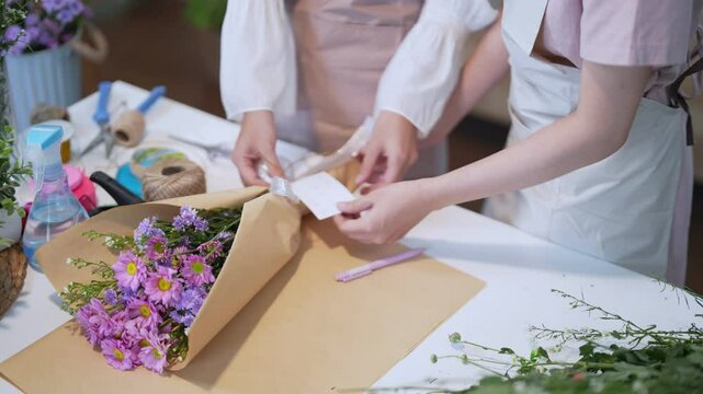 Two florists writing a greeting card to accompany a flower bouquet, adding a personal touch to their floral arrangement.