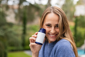 Woman smiling and holding a pill blue bottle with blank label, with empty space