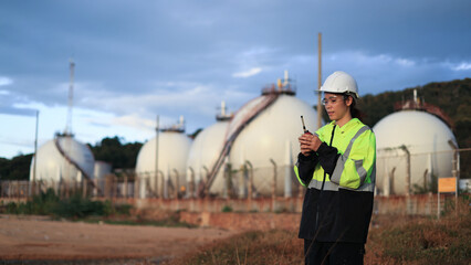 A female engineer with a green safety jacket holding walkies talkies checking on the site of the Petrochemical plant