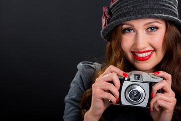 Vintage retro style portrait of beautiful smiling young woman holding an old film camera.