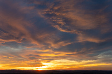 Obraz premium Sunset illuminates the sky with vibrant colors over a tranquil landscape during golden hour