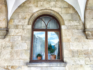 Historic stone building showcases an elegant arched window with potted plants and curtains in a...