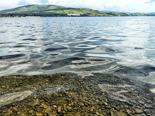 Rippling water reflecting hills under a cloudy sky at a serene lakeside location