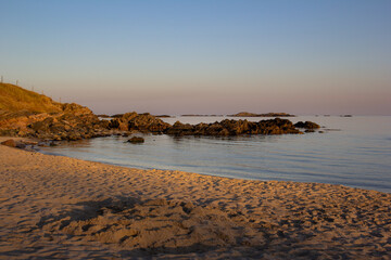 Serene beach at sunset with calm waters and rocky coastline in the background.
