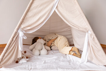 Happy little caucasian boy is lying in a wigwam. Childhood, playing with soft toys, tenderness....