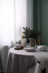 A Cozy Table Setting with plates, teapot, vase with green spruce on light round table . High quality photo.