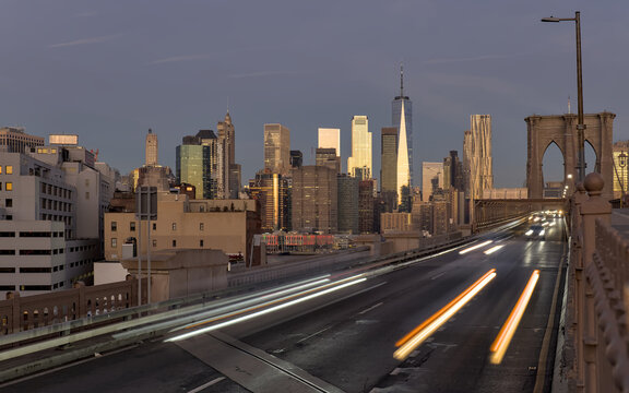 cars driving over the brooklyn bridge from manhattan new york city (long exposure light trails) traffic commute commuters traveling to work jobs (skyline background at dawn sunrise) dark night time