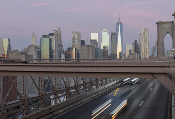 Naklejka premium cars driving over the brooklyn bridge from manhattan new york city (long exposure light trails) traffic commute commuters traveling to work jobs (skyline background at dawn sunrise) dark night time