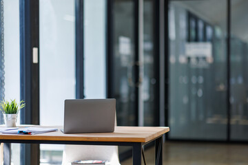 Laptop Computer, notebook, and eyeglasses sitting on a desk in a large open plan office space after working hours	