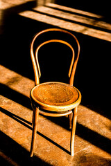 Elevated view of an old vintage cafe chair in a large empty room, with morning sunlight coming in through the windows and creating long dark shadows on floor.