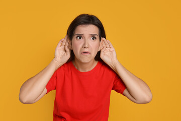 Woman showing hand to ear gesture on orange background