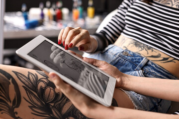 Tattoo artist showing tablet with sketch to client in salon, closeup