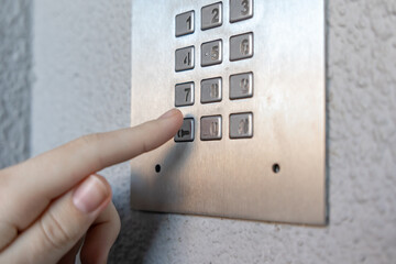 Finger pressing metallic keypad on secure access control panel mounted on textured white wall for residential building entry