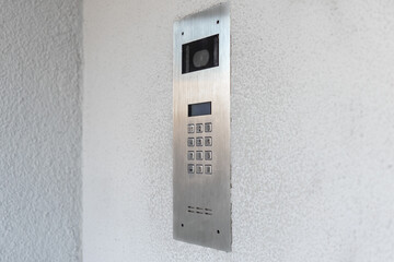 Modern intercom system with camera and keypad on textured white wall for secure building access...