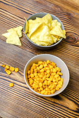 Crispy salt snacks, chips, nut, corn in bowl on wooden background close up. Unhealthy junk food, bar drink party concept, close up vertical