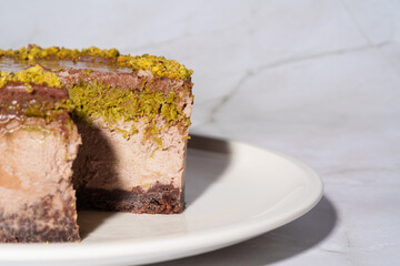 Close up Dubai chocolate cheesecake with pistachio paste and kataifi dough covered in chocolate ganache on white plate. White background with copy space. Indulgence, gourmet desserts, art of culinary