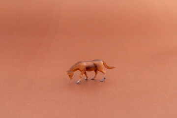 A single brown horse plastic toy grazing on brown background