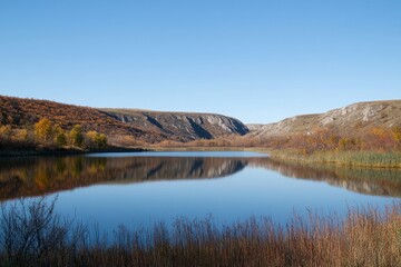In a peaceful valley, tranquil waters mirror the vibrant colors of autumn foliage, all beneath a stunningly clear blue sky
