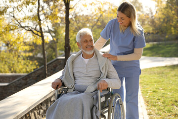 Caregiver assisting senior man on wheelchair in park. Home health care service