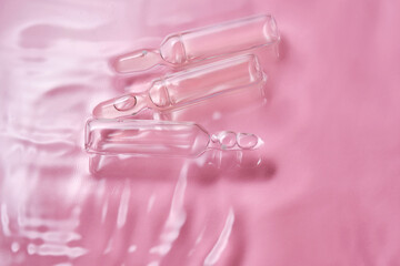 Ampoules in water on a pink background.