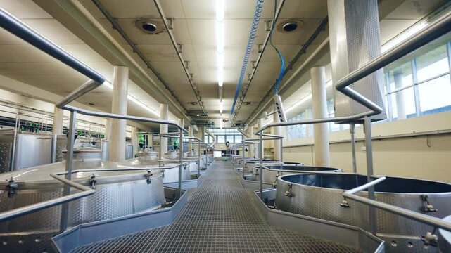 Pass between the rows of stainless clean tanks for wine production, metal barrels for fermentation, distillation and filtration process, high quality wine production on factory