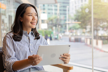 close up manager businesswoman hold digital tablet and looking away through glass window while sit in the office private room for relax or thinking about new business project for startup 