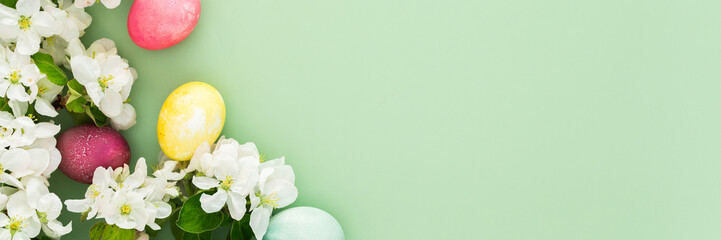 Spring Easter background, multi-colored Easter eggs and blooming apple tree branches on a green background, copy space, banner