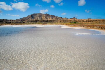 A vast and serene salt pan reflecting sunlight under a bright blue sky, located in the Salinas of Cape Verde.
