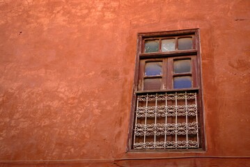 Rustic window with decorative iron bars on a warm-toned brick wall, showcasing vintage architecture.