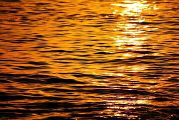 Close-up of shimmering golden ripples on the water's surface, illuminated by the setting sun,...
