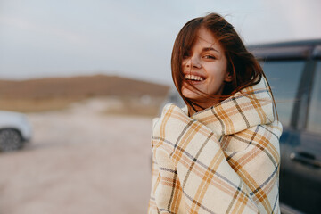 Woman standing in blanket by car on roadside during travel adventure in nature beauty