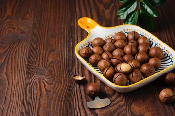 Healthy snack, macadamia nuts in shell in rectangular ceramic plate on brown wooden background. Nuts from around the world. Healthy food.